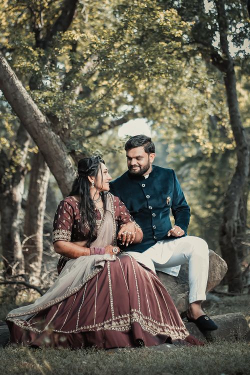 Free A couple in traditional attire poses romantically outdoors, surrounded by trees. Stock Photo
