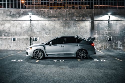 Free A silver sports car parked in a dimly lit city parking lot at night, showcasing urban lifestyle. Stock Photo