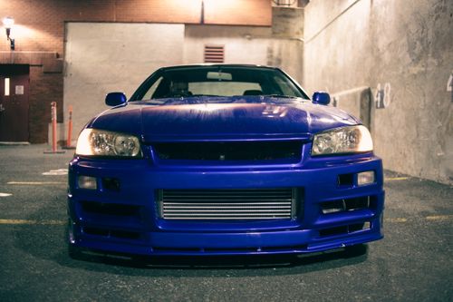 Free Front view of a vibrant blue sports car parked outdoors, illuminated by urban lighting. Stock Photo