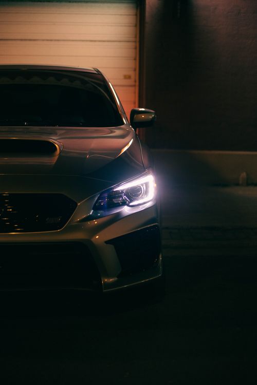 Free Close-up of a sleek sedan's headlight glowing in the dark, showcasing modern automotive design. Stock Photo