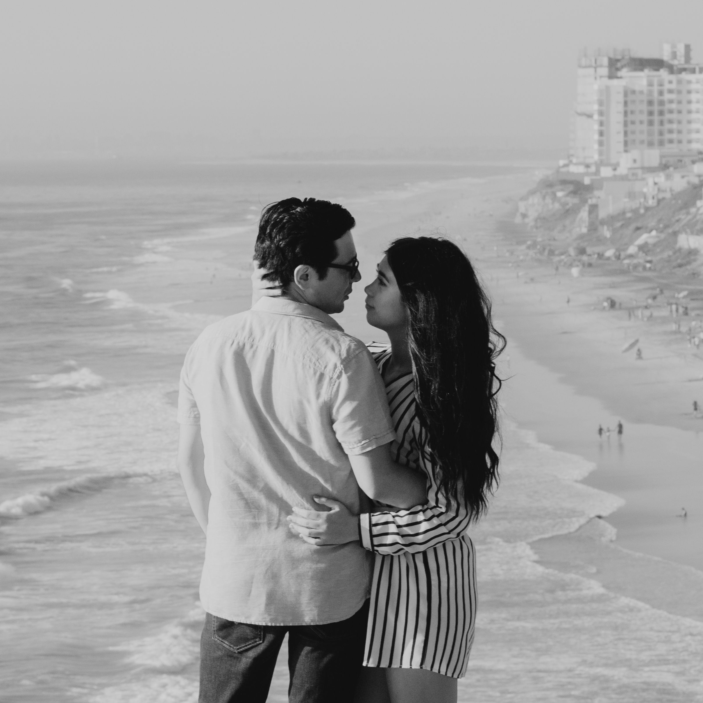 A loving couple shares an embrace by the ocean, capturing an intimate moment in monochrome.