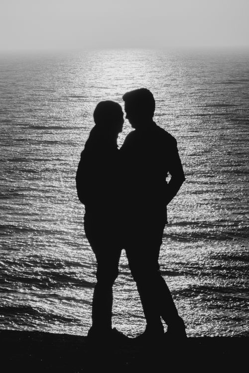 Free Silhouette of a romantic couple standing close by the seaside during sunset. Stock Photo