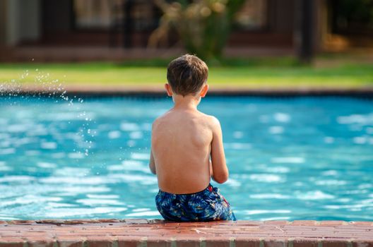 A child sits on the poolside, enjoying a sunny day outdoors.