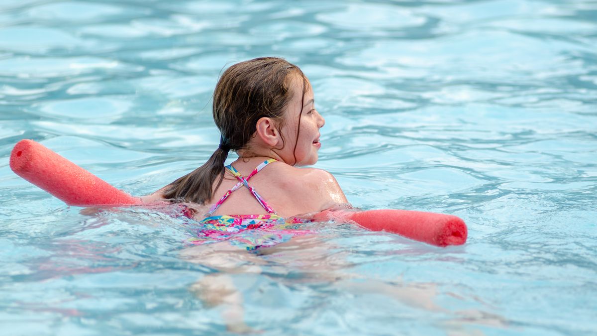 Girl swimming in a pool with a red pool noodle