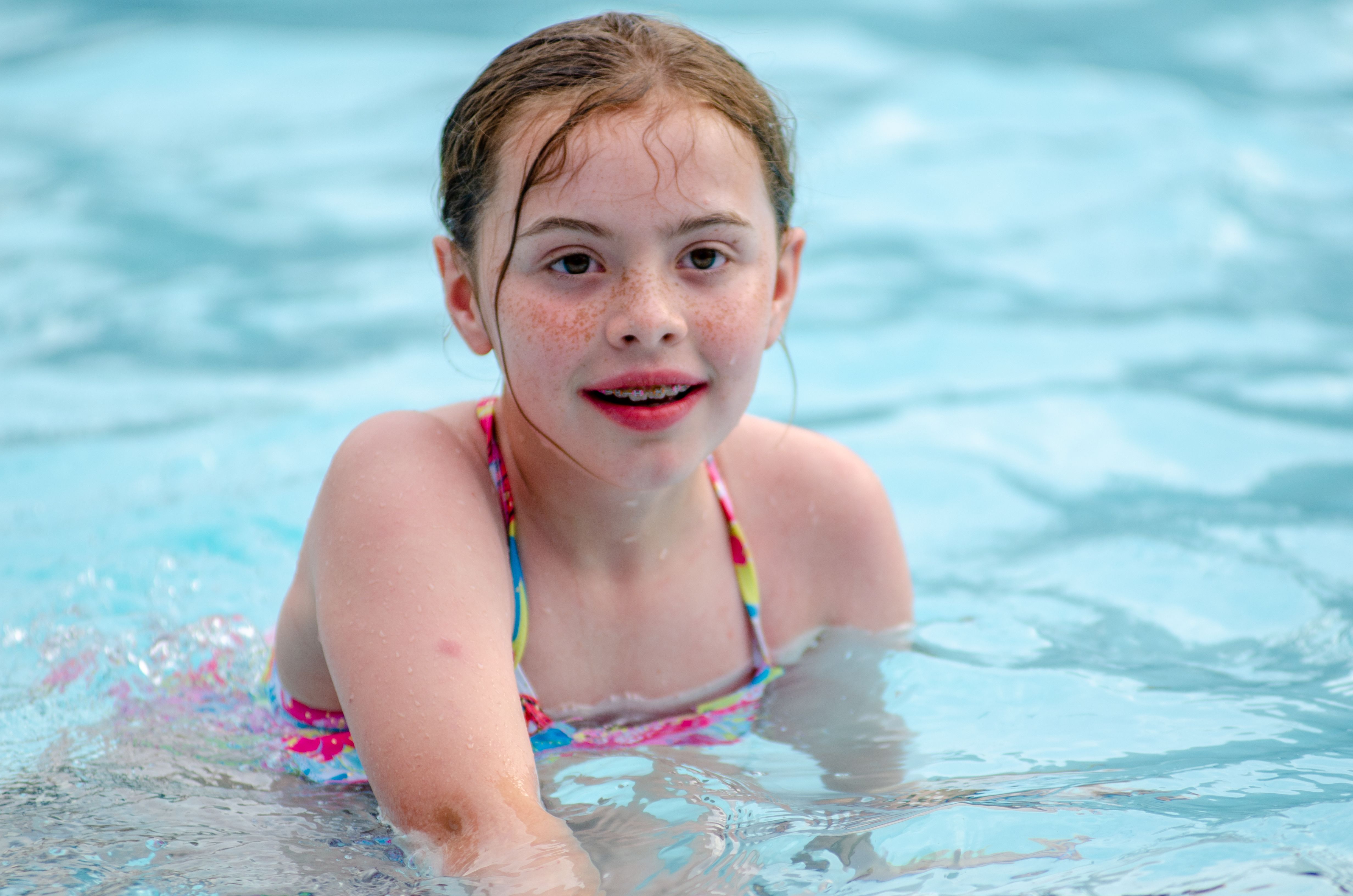 A young girl with freckles having fun swimming in a clear blue pool.