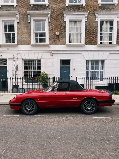 Vintage red convertible parked in front of Georgian townhouses in London.