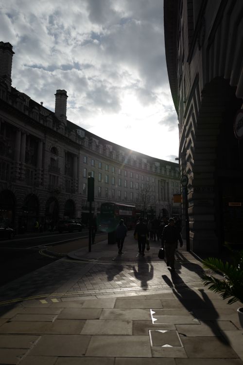 Free People walking on a historic urban street with long shadows at sunset, architectural detail visible. Stock Photo