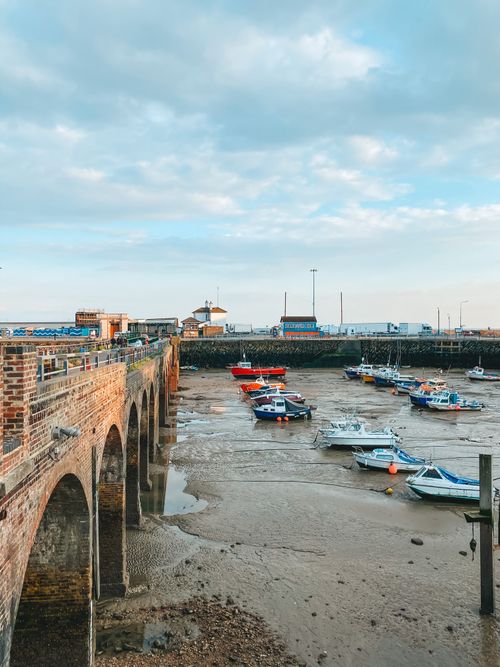 Free A scenic view of a harbor at low tide with boats docked and a historic brick bridge. Stock Photo