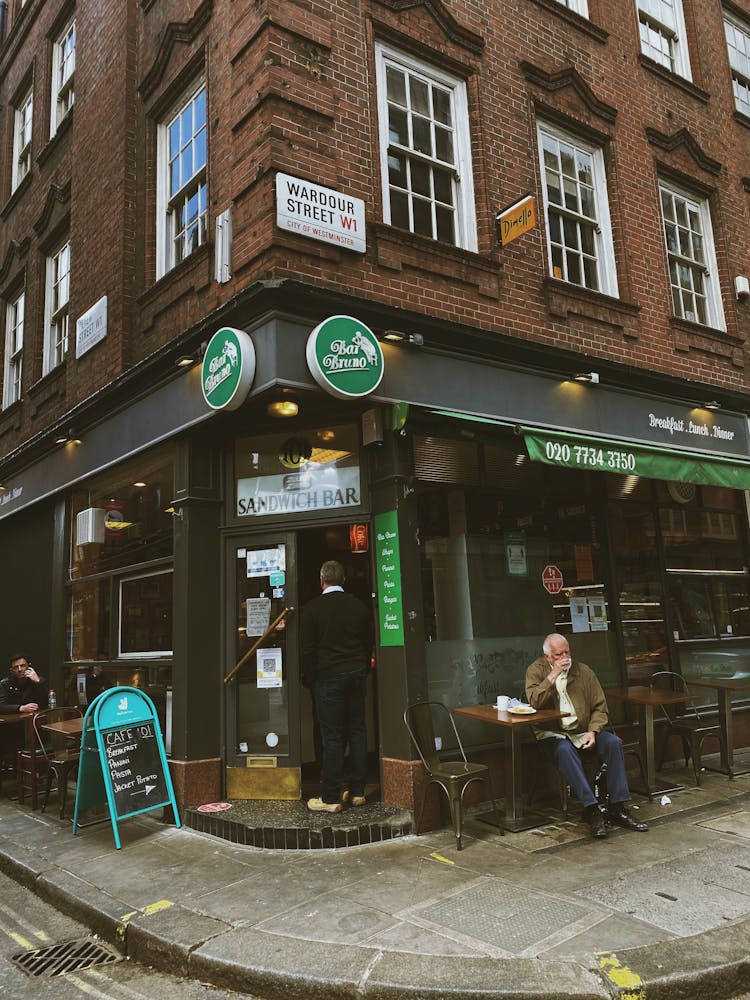 Senior Man Sitting By Sandwich Bar On Corner Of Building