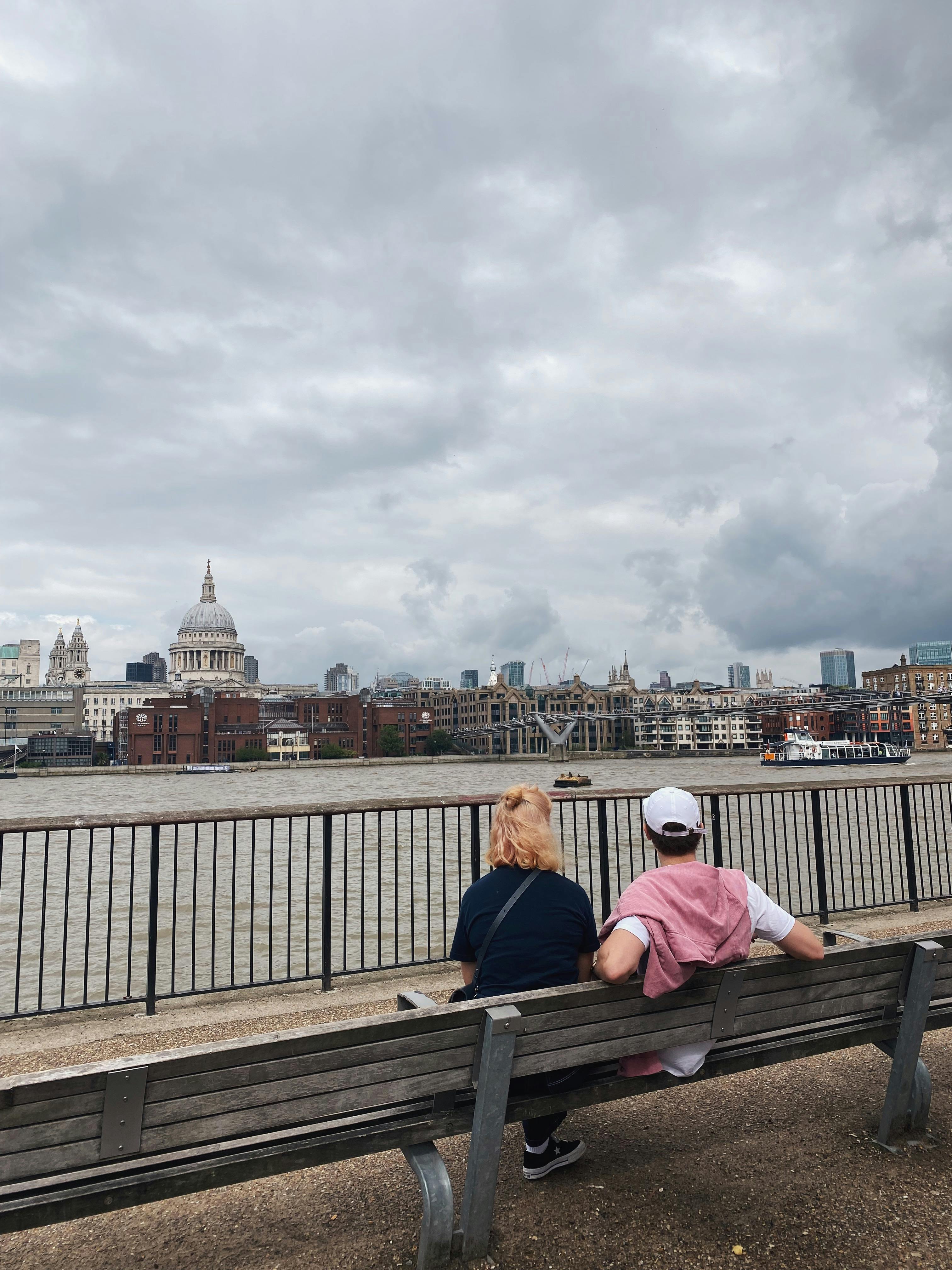 A couple sits on a bench overlooking the River Thames and St. Paul's Cathedral in London.
