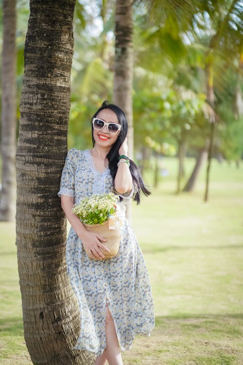 Smiling Woman Holding a Bag of Flowers and Leaning on a Tree Trunk