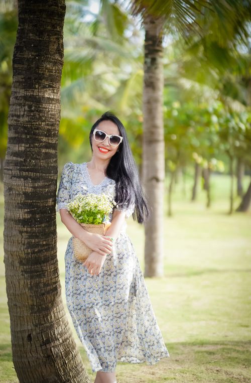 Free Smiling woman with floral dress and flowers enjoys tropical setting under palm trees. Stock Photo