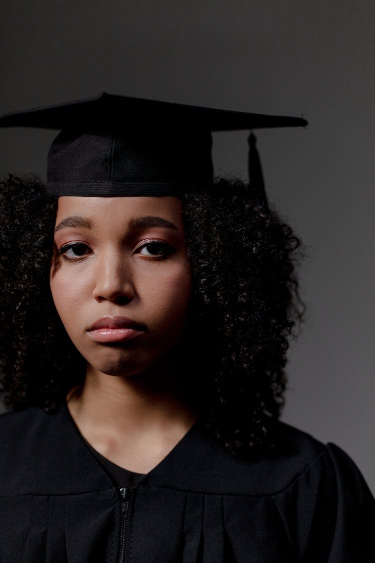 A Close Up On A Sad black Female Student Looking At Camera And Wearing Square Academic Cap