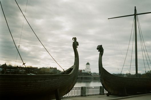 Two traditional wooden Viking ships by the harbor in Vyborg, Russia, captured under a cloudy sky.
