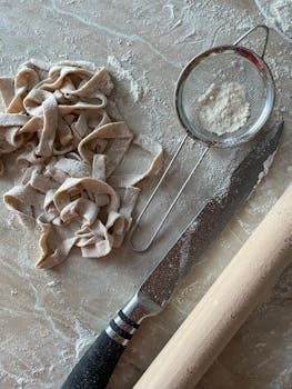 Top view of fresh homemade pasta with kitchen tools on a floured surface, showcasing the art of cooking.