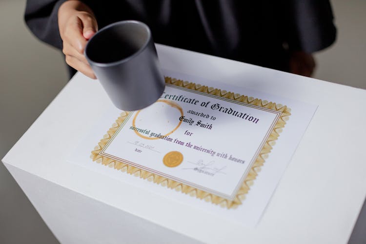 A Person Holding A Mug Near The Certificate On The Table