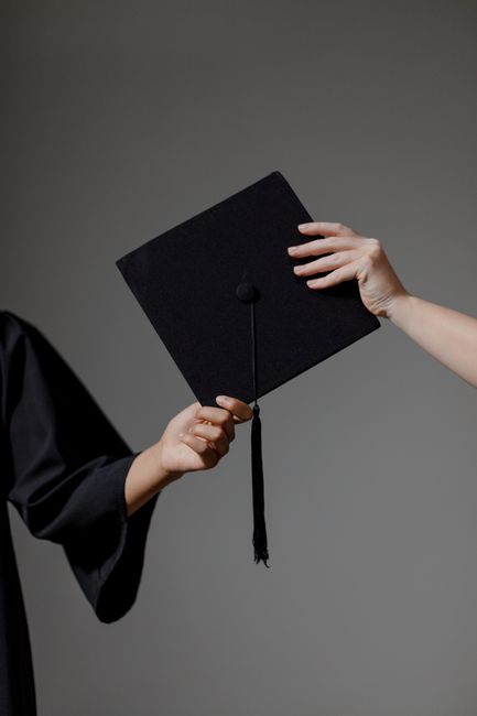 Two people exchanging a graduation cap on a grey background, symbolizing achievement. Two people exchanging a graduation cap on a grey background, symbolizing achievement.