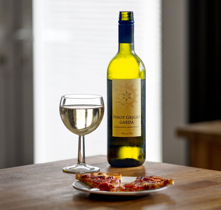 A Wine Glass And Bottle Near The Pizza On A Ceramic Plate