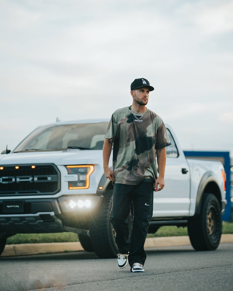 Young Man In Cap Walking In Front Of White Pickup