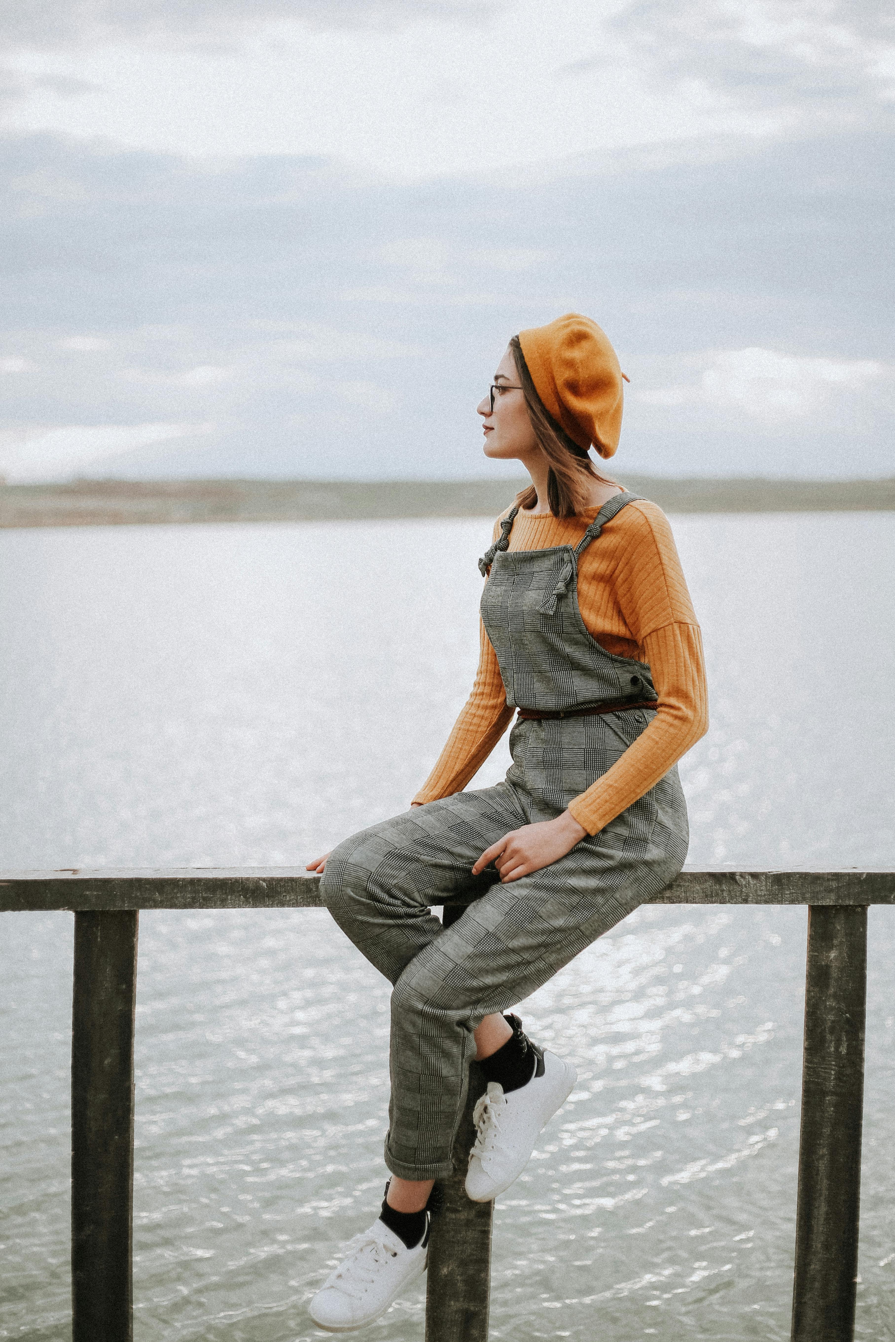 Woman in fashionable outfit admiring lake view, wearing a beret and dungarees.