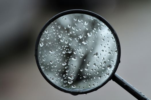 Close-up of dewdrops on a round rearview mirror capturing a rainy mood.