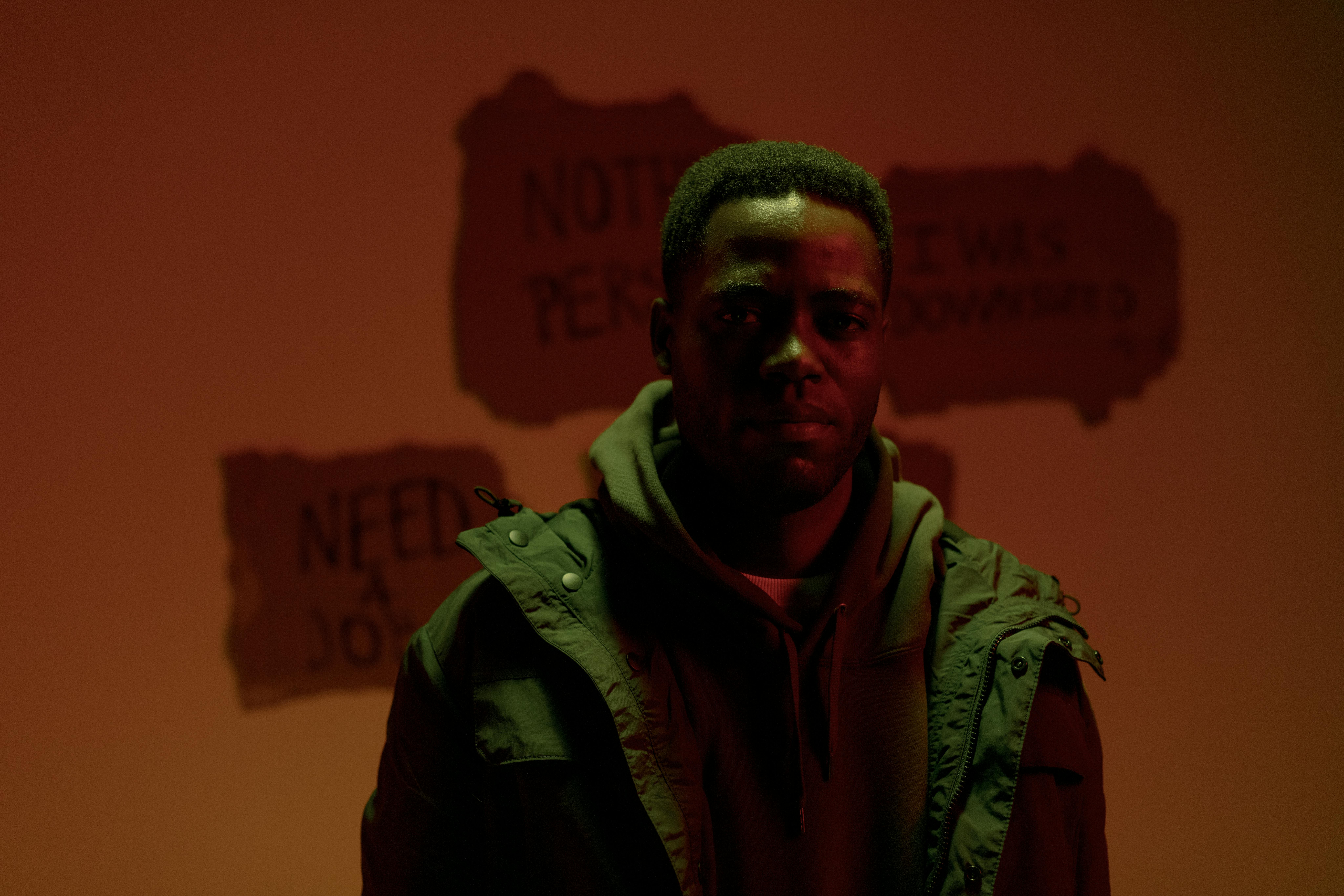 A man standing indoors with signs about unemployment in a moody atmosphere.