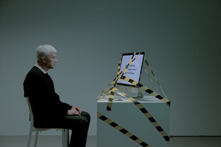 Elder Man Sitting In Front Of A Computer Tied With Black And Yellow Tape