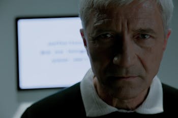 Elderly man looking at camera and behind him screen saying that he is no more needed