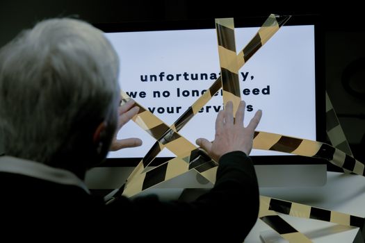 An elderly man reacts to a dismissal message on a computer, conveying ageism and unemployment themes.