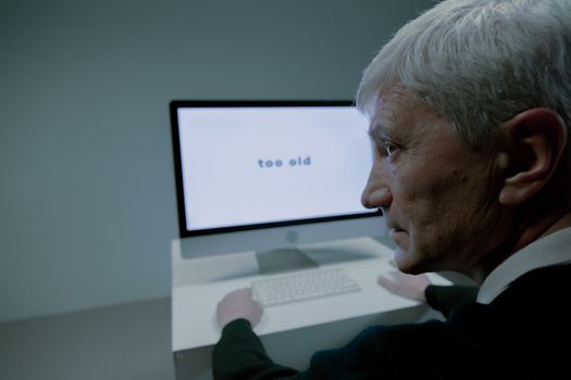 Senior man confronted with ageism on computer screen in job search.