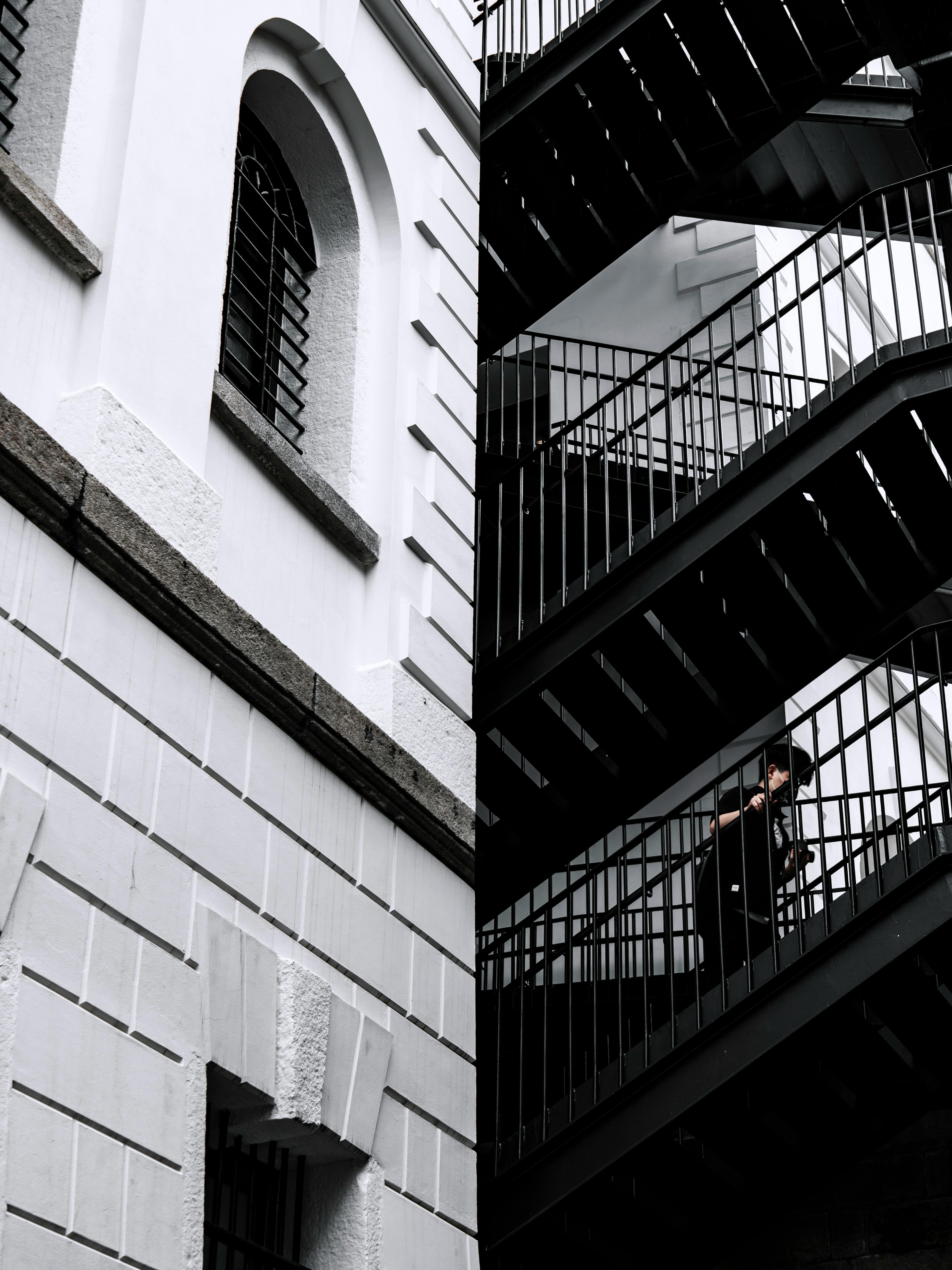 Black and white image of a person ascending a staircase on a building in Hong Kong, showcasing urban architecture.