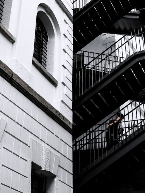 Black and white image of a person ascending a staircase on a building in Hong Kong, showcasing urban architecture.