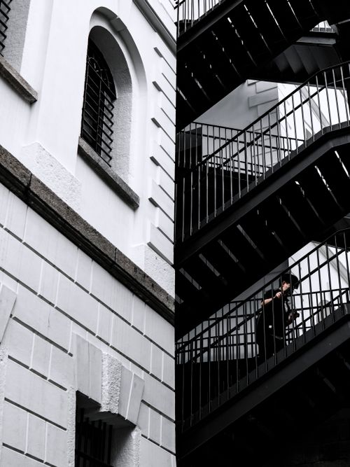 Free Black and white image of a person ascending a staircase on a building in Hong Kong, showcasing urban architecture. Stock Photo