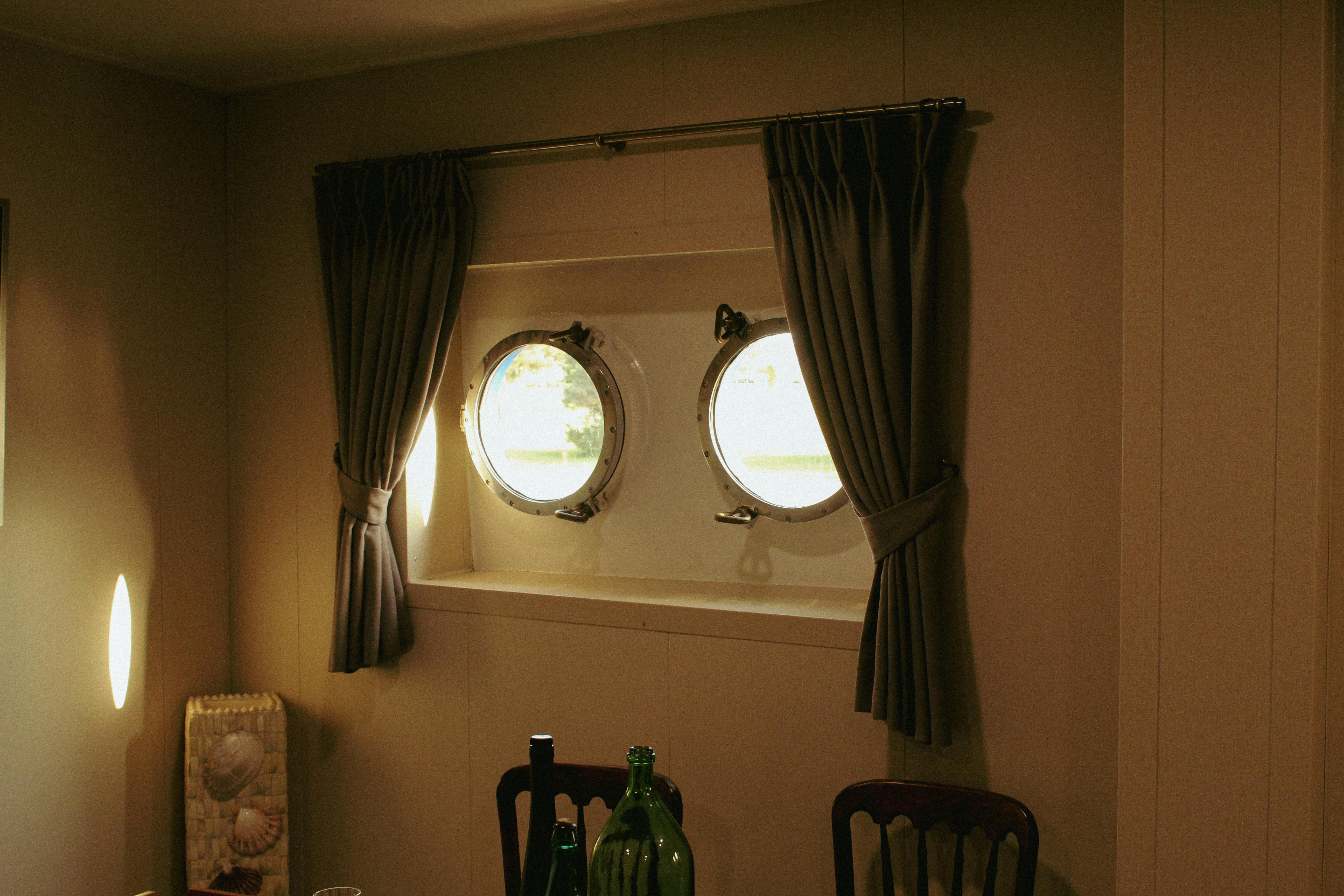 furniture shipping - Warm ship cabin interior featuring round porthole windows with curtains and nautical decor.