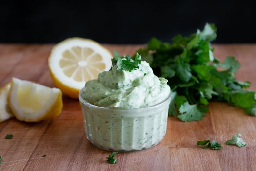 Close-up of creamy cilantro lemon dip in a ramekin with fresh ingredients on a wooden table.