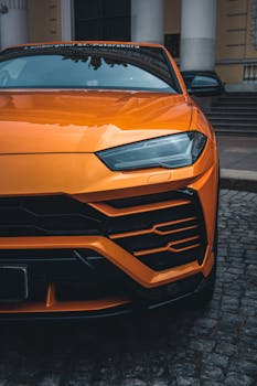 Close-up of an orange Lamborghini SUV parked on cobblestone pavement.