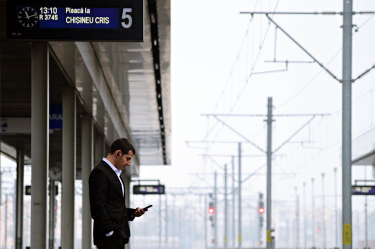 A Man In Black Suit Using His Phone While Waiting On Train Station