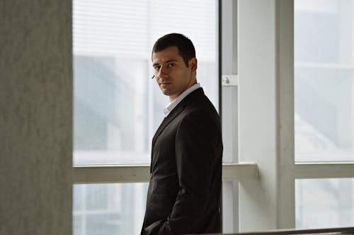 A Man in Black Suit Standing Near the Window