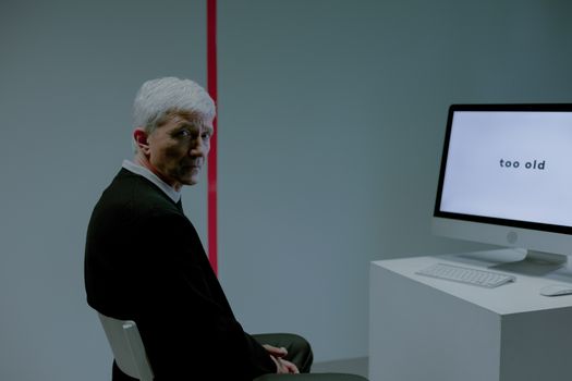 Senior man in a modern office setting facing age bias on-screen message 'too old'.