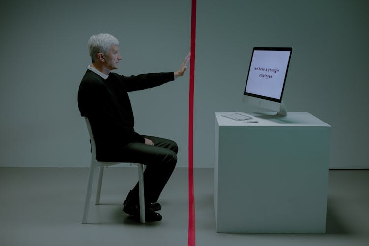 Senior Adult Man Sitting Before Computer Separated From Him By Red Line