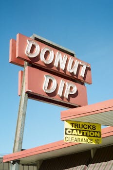 Retro donut shop sign with caution notice against a clear blue sky.
