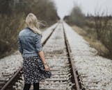 一位年轻的金发女子行走在户外的铁轨上，展现出自由与旅行癖