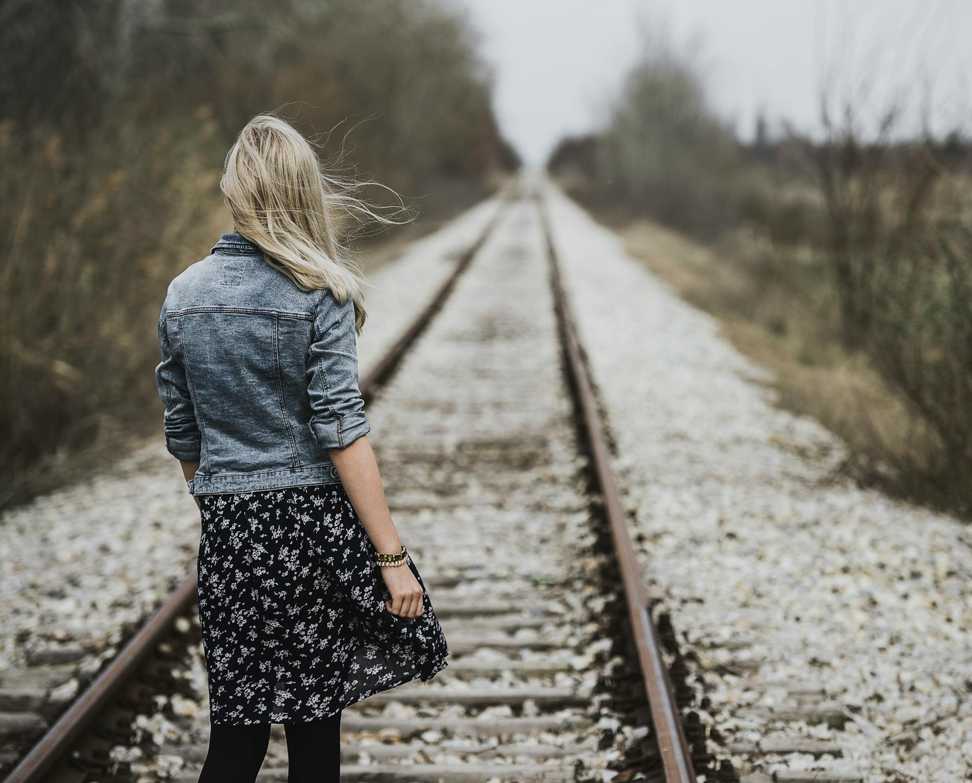 A young woman with blonde hair walking on railroad tracks outdoors, embodying freedom and wanderlust.