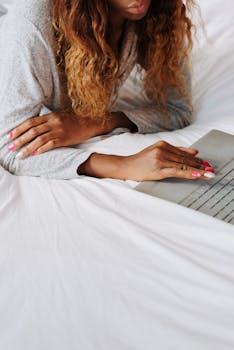 Woman with curly hair using a laptop on a bed, enjoying a relaxed morning.