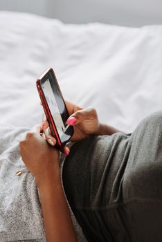 Close-up of a woman using a smartphone while relaxing in bed, capturing a cozy morning moment indoors.