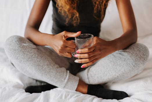 A woman sitting cross-legged holding a coffee cup in a peaceful bedroom setting.