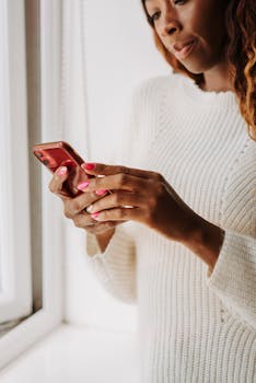 Casual woman browsing on her smartphone near a window indoors.