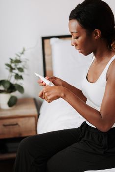 Woman with curly hair applies skincare cream while sitting in a bedroom. Calming and personal self-care moment.