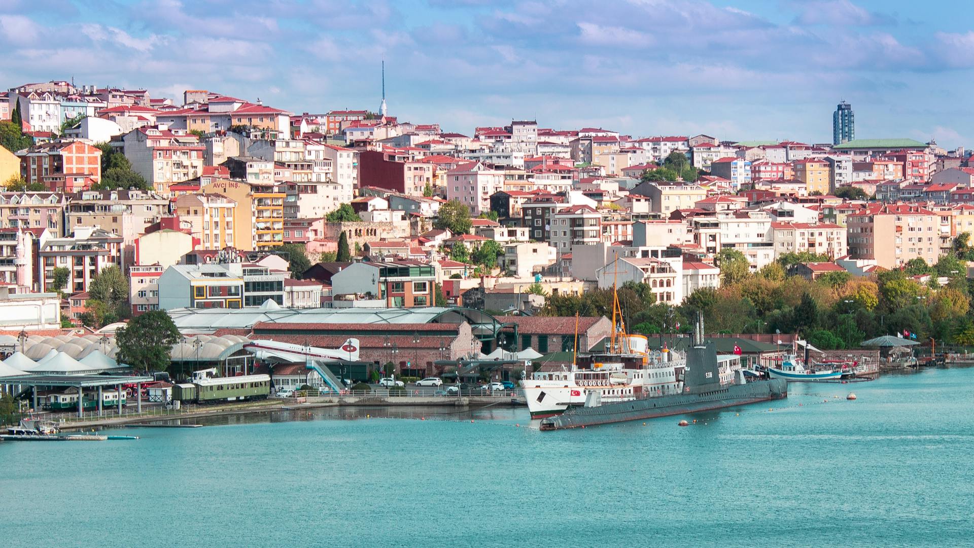 A panoramic view of colorful buildings overlooking a harbor with ships in a bustling city.