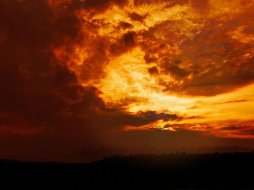 Free A mesmerizing sunset with vivid orange clouds casting a warm glow over a silhouetted landscape. Stock Photo